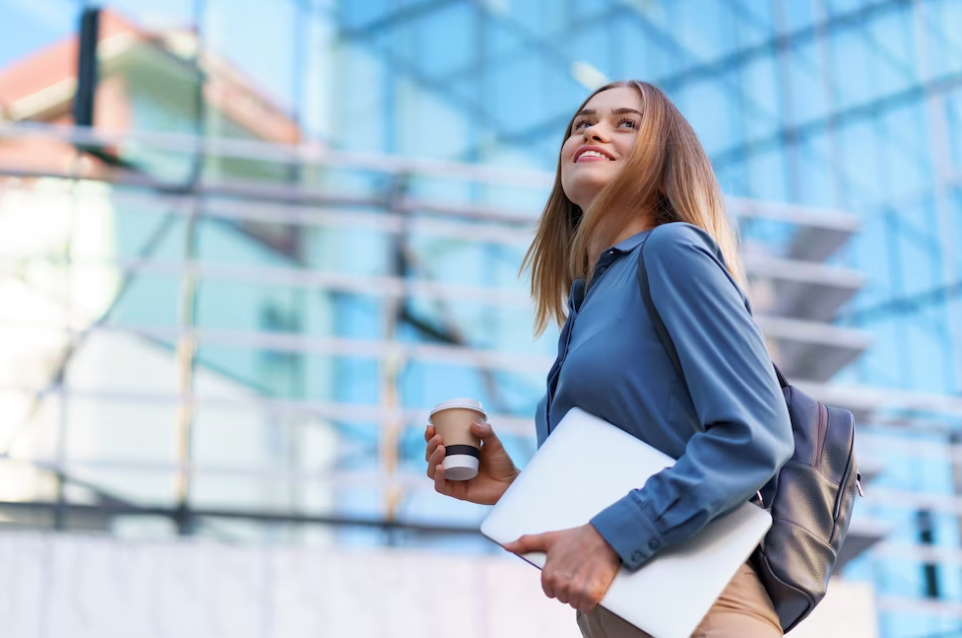 woman holds coffee and laptop near the buildings